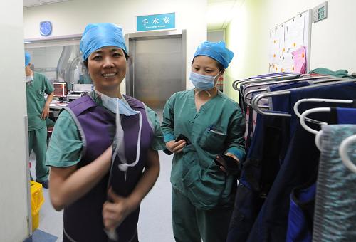 河南省人民医院心脏内科主任医师李牧蔚(左)在铅衣架前穿上铅衣准备手术(5月8日摄)。新华社记者 赵鹏 摄